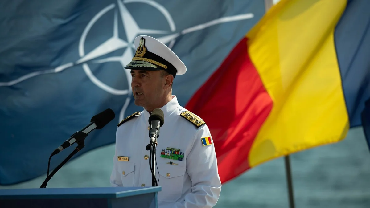 Viceamiralul Mihai Panait, șeful Statului Major al Forțelor Navale, vorbind la un pupitru, între drapelul NATO și cel al României (fotografie de arhivă de la Ziua Marinei, Constanța, august 2024)