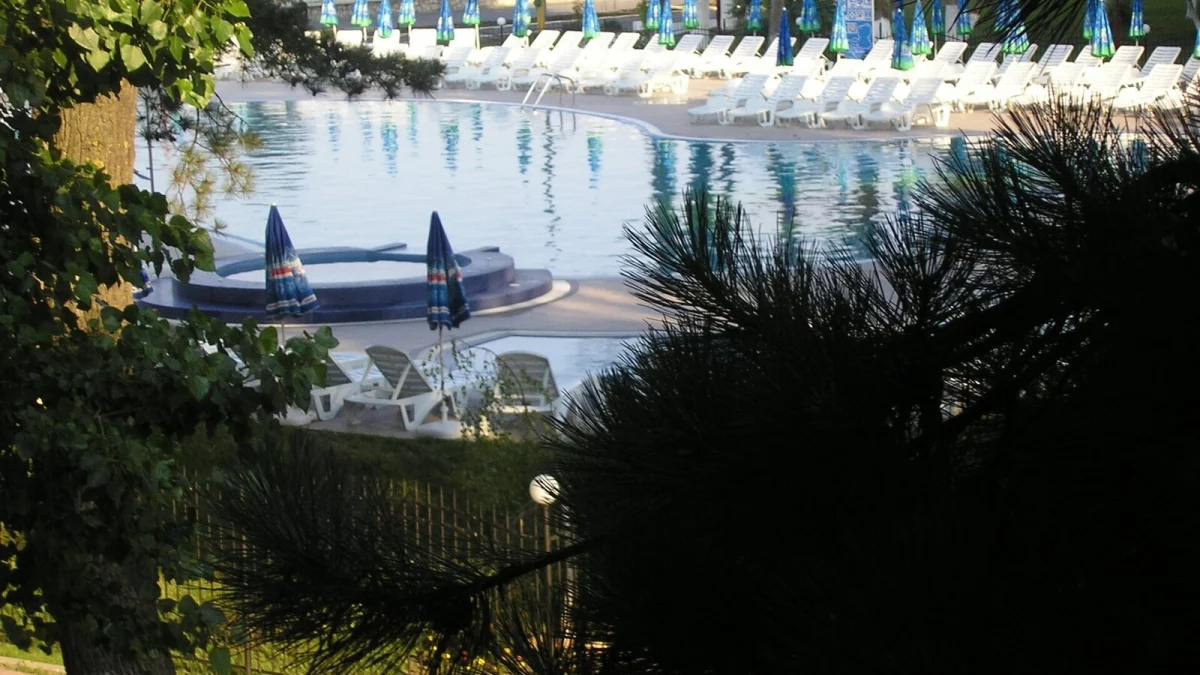Piscină cu șezlonguri și umbrele strânse într-un complex hotelier din Mamaia, văzută printre pini (fotografie de arhivă din alt complex, imagine ilustrativă)