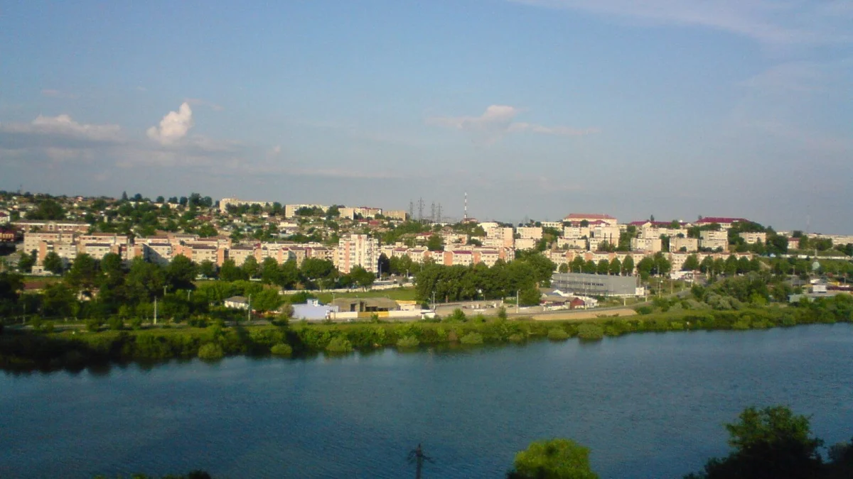 Orașul Cernavodă văzut de peste apă, cu blocuri și case pe deal, într-o zi senină (fotografie de arhivă)