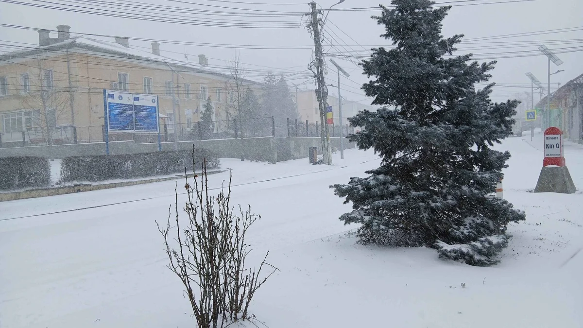 Centrul localității Băneasa, județul Constanța, în ninsoare, cu o clădire administrativă și bornă kilometrică „Km 0” (fotografie de arhivă din februarie, imagine ilustrativă, nu arată clădirea centrului)