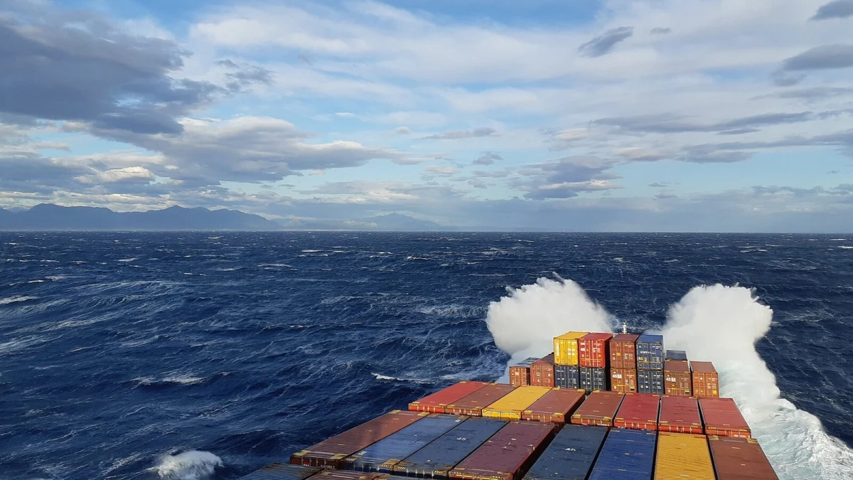 Prova unei nave de containere pe mare agitată, cu stive de containere colorate și stropi de valuri (imagine ilustrativă, nu este nava Contship Jet)