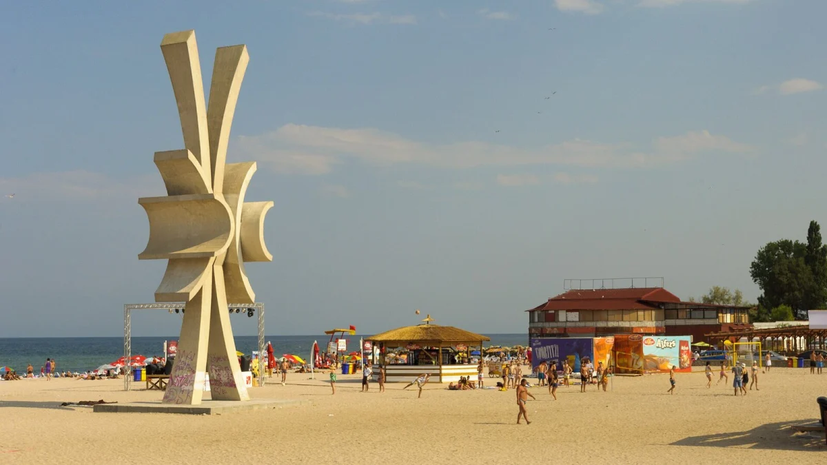 Plaja din Costinești cu sculptura în formă de soare, turiști și un chioșc acoperit cu stuf (fotografie de arhivă, imagine ilustrativă)