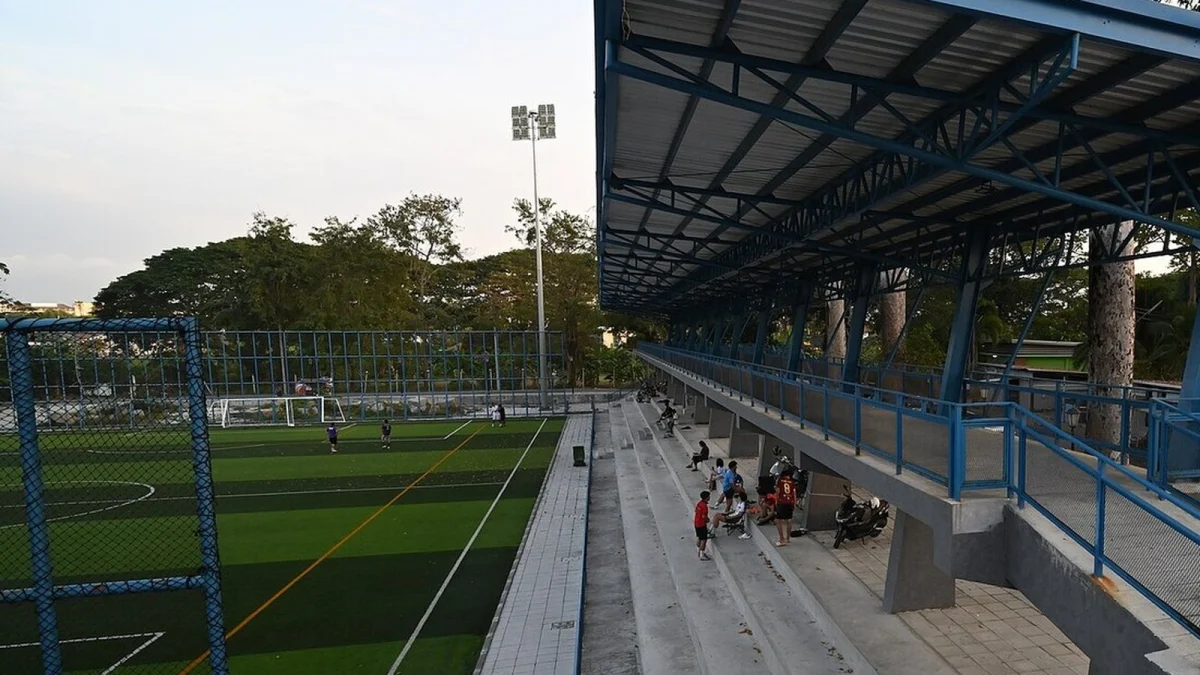 Teren de fotbal cu gazon artificial și o tribună acoperită, cu câțiva spectatori, la apus (imagine ilustrativă, nu este din România)