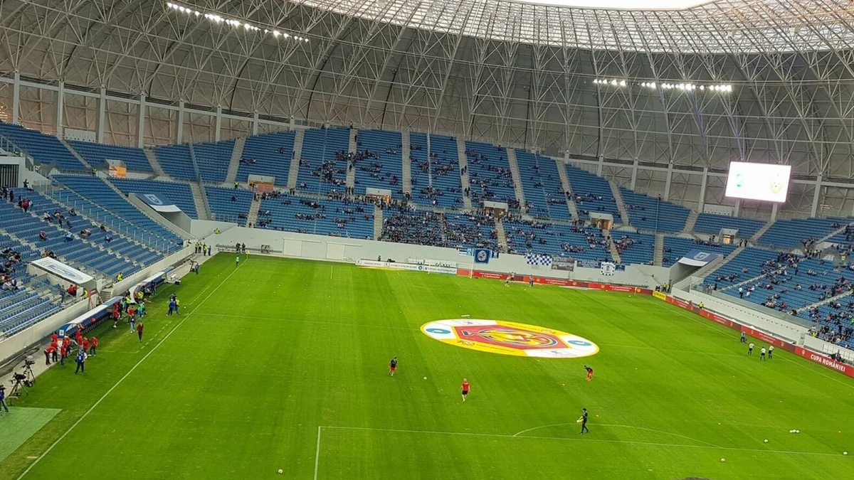 Interiorul stadionului Ion Oblemenco din Craiova, cu tribune albastre, acoperiș metalic și jucători la încălzire pe gazon (fotografie de arhivă, 2018)