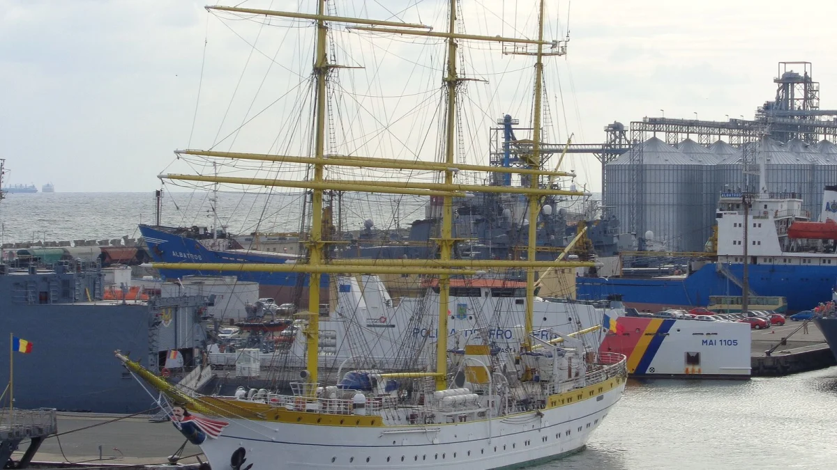 Nave la chei în Portul Constanța, cu silozuri de cereale în fundal și o navă-școală cu trei catarge în prim-plan (fotografie de arhivă, 2014)