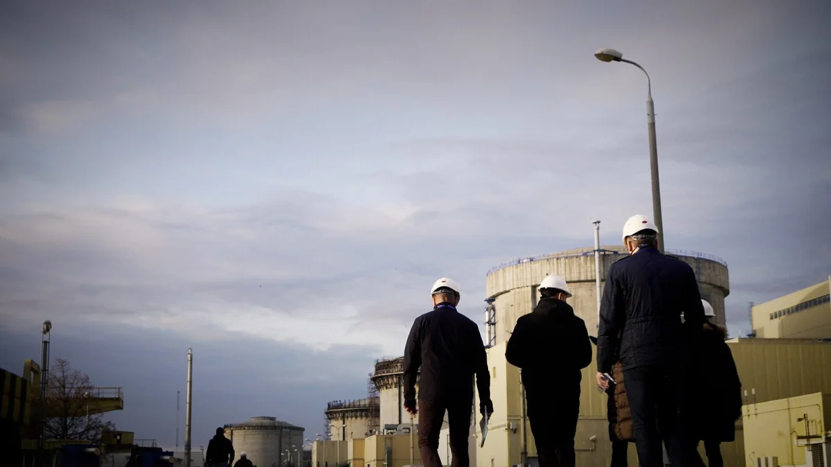 Oameni cu căști de protecție, văzuți din spate, pe platforma centralei nucleare de la Cernavodă, cu clădirile reactoarelor în fundal (imagine ilustrativă, arhivă IAEA, decembrie 2024)