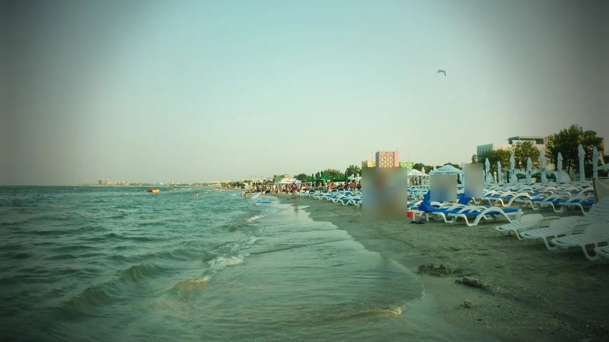 Plaja din Mamaia cu șezlonguri albastre și albe, valuri mici și clădiri de pe litoral în depărtare (fotografie de arhivă, imagine ilustrativă, nu arată Hotelul Select)