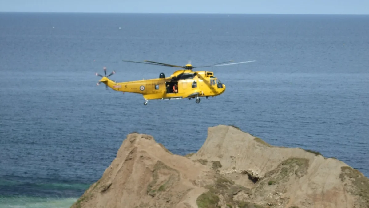 Elicopter galben de căutare și salvare zburând deasupra mării, lângă o stâncă (imagine ilustrativă, Marea Britanie, 2014, nu este elicopterul care a participat la căutările din Marea Neagră)