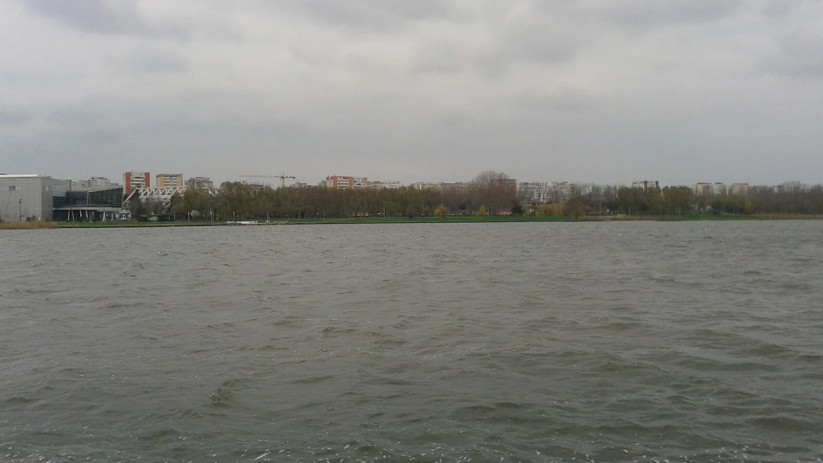 Lacul Tăbăcăriei din Constanța, cu malul verde, parcul și blocurile în fundal, sub un cer noros (fotografie de arhivă, imagine ilustrativă, nu arată terenurile expropriate)