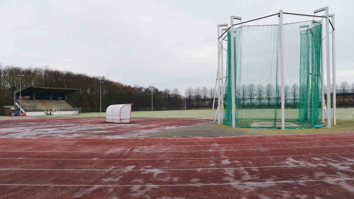 Pistă de atletism cu zăpadă topită, tribună mică și plasă de protecție pentru aruncări, într-o zi cenușie (imagine ilustrativă, nu este din Constanța)