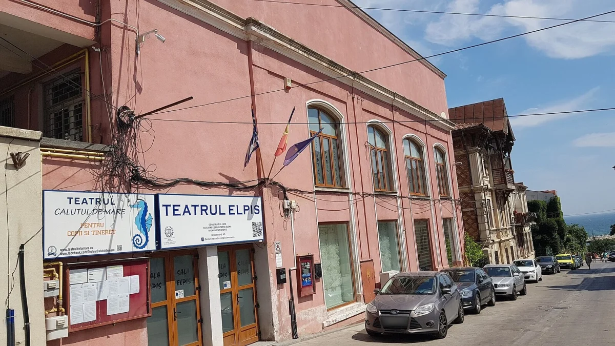 Clădirea roz a Teatrului Elpis din Constanța, sediul Teatrului pentru Copii și Tineret „Căluțul de mare”, cu panouri la intrare și mașini parcate pe stradă (fotografie de arhivă, 2018)