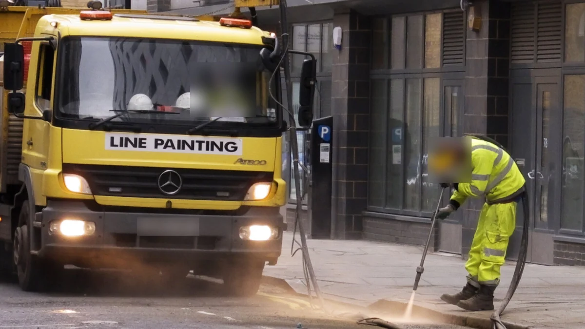Camion pentru marcaje rutiere și un muncitor în echipament reflectorizant care curăță carosabilul înainte de trasarea liniilor (imagine ilustrativă, Londra, 2016)