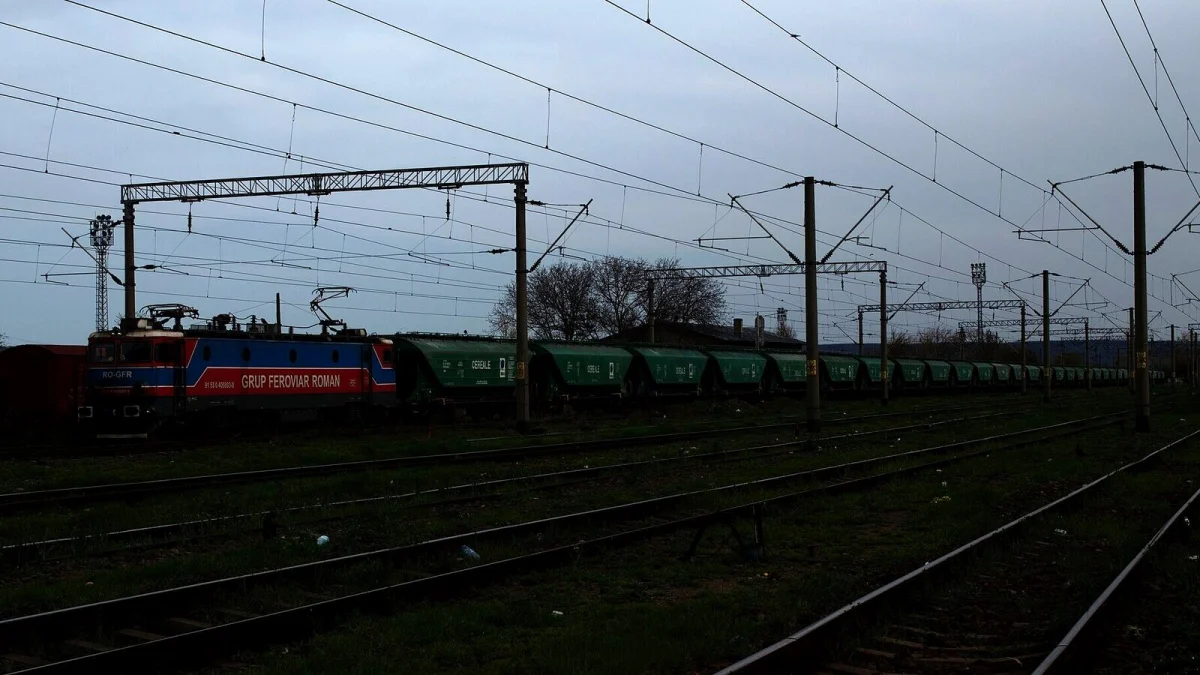 Locomotivă Grup Feroviar Român cu un șir lung de vagoane verzi pentru cereale vrac inscripționate „Cereale”, într-o stație CFR (fotografie de arhivă, Adjud, 2023, imagine ilustrativă)
