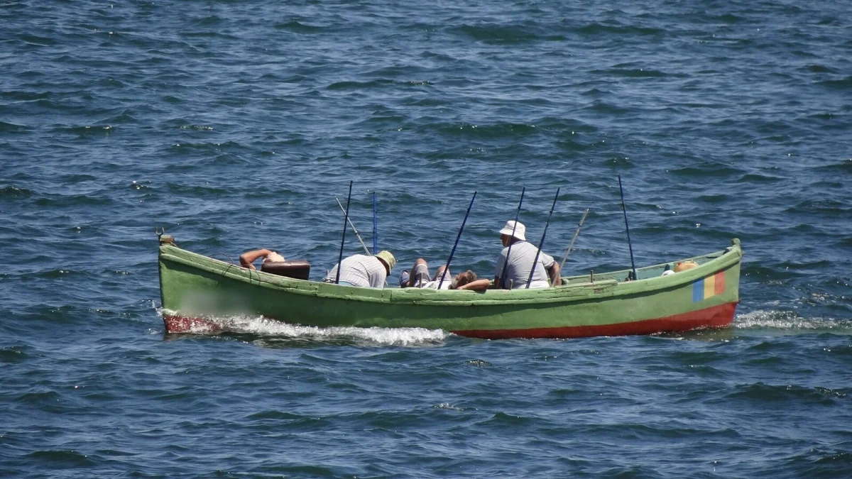 Barcă de pescari verde pe marea albastră, în largul falezei din Constanța, cu mai mulți pescari și undițe (fotografie de arhivă)